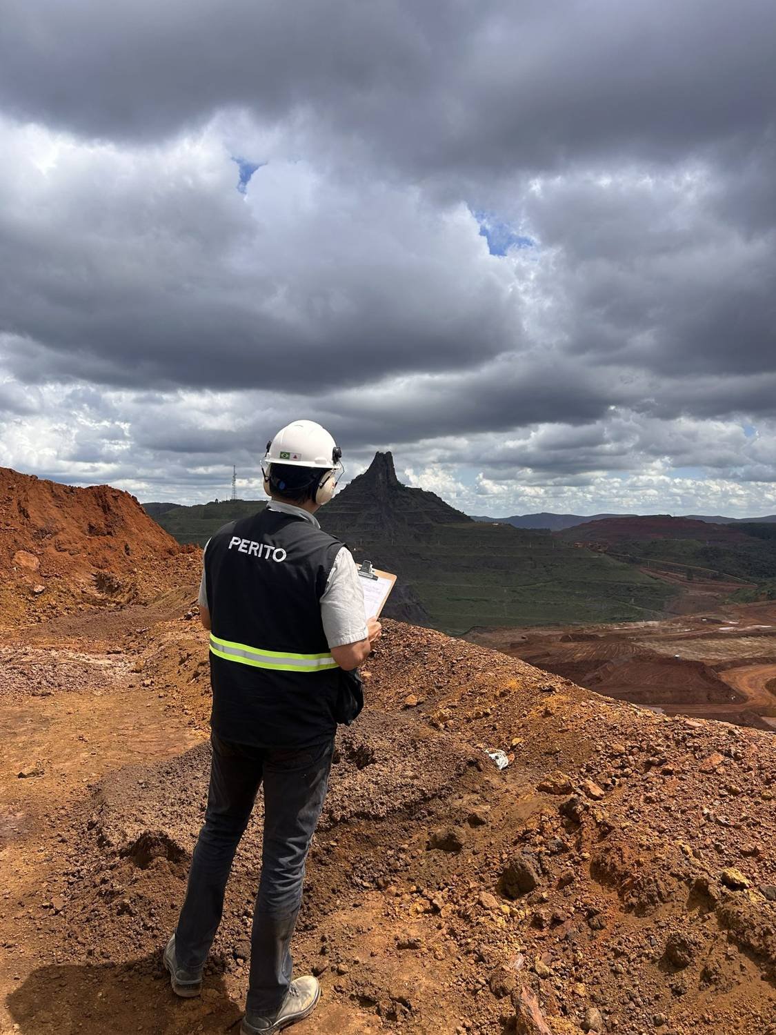 Perito em diligência sobre cava de mineração, com prancheta e protetor auricular