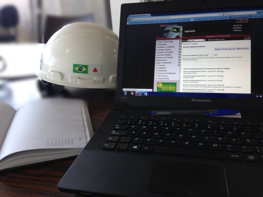 Capacete de segurança ao lado de notebook aberto nas Normas Regulamentadoras